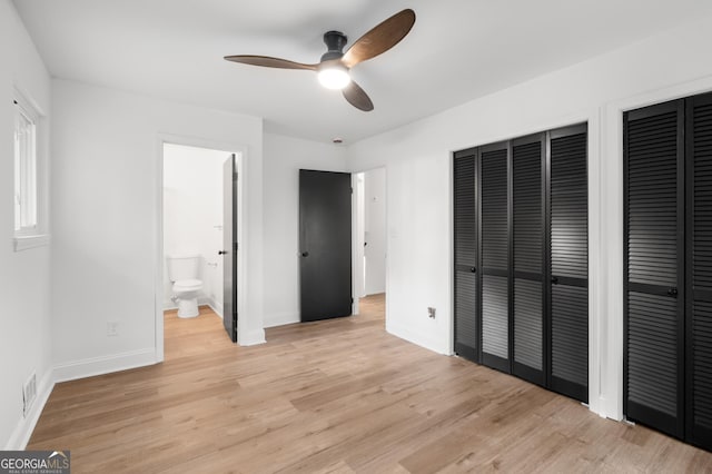 unfurnished bedroom featuring light wood finished floors, ensuite bath, multiple closets, baseboards, and visible vents