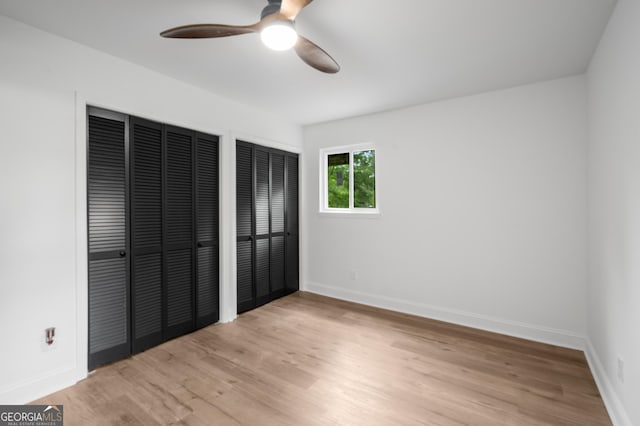 unfurnished bedroom featuring two closets, a ceiling fan, baseboards, and light wood-style floors