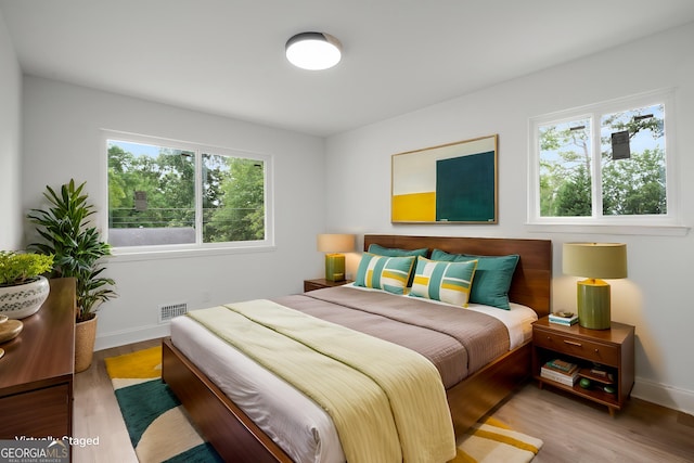 bedroom with baseboards, visible vents, multiple windows, and wood finished floors