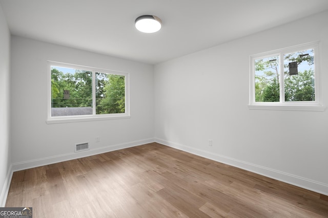 unfurnished room featuring a healthy amount of sunlight, baseboards, wood finished floors, and visible vents