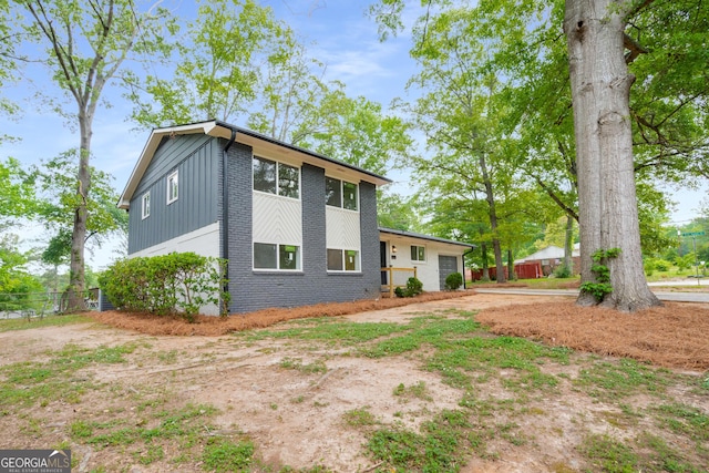 view of front of house with board and batten siding, brick siding, fence, and a garage