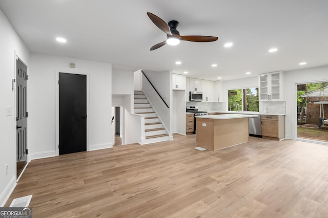 kitchen featuring ceiling fan, light wood-style floors, stainless steel appliances, a kitchen island, and glass insert cabinets