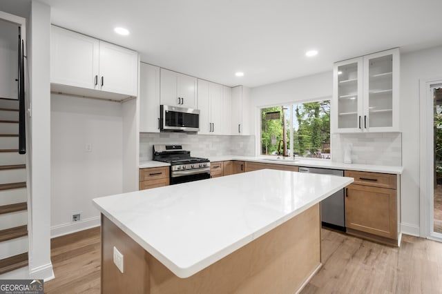 kitchen with a sink, light wood-style flooring, stainless steel appliances, backsplash, and glass insert cabinets