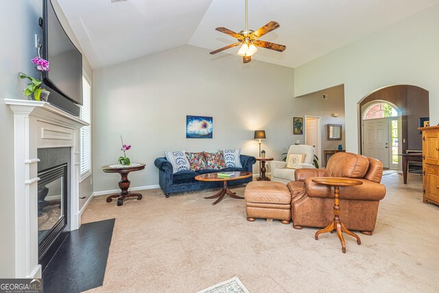 living room featuring light carpet, high vaulted ceiling, ceiling fan, a fireplace with flush hearth, and arched walkways