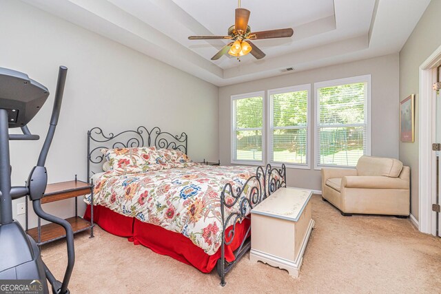 bedroom featuring light carpet, a raised ceiling, and ceiling fan