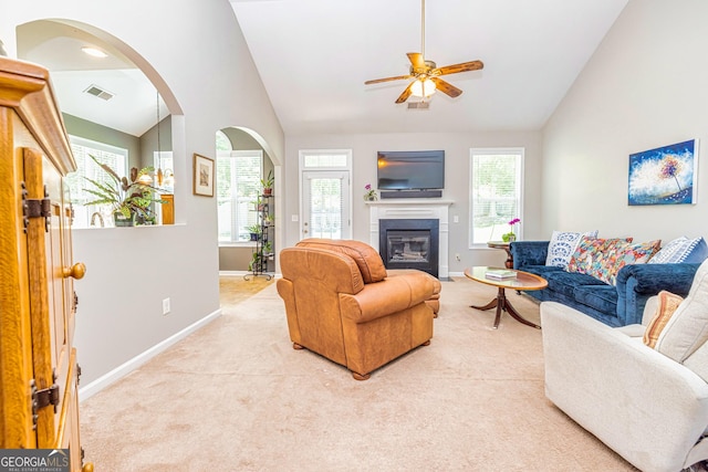living room with baseboards, ceiling fan, light colored carpet, a glass covered fireplace, and high vaulted ceiling