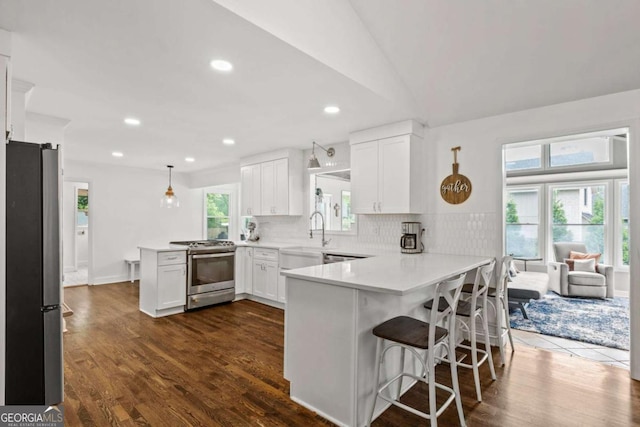 kitchen featuring a peninsula, white cabinets, a sink, appliances with stainless steel finishes, and backsplash