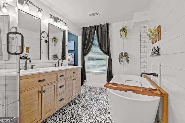 full bath featuring a sink, a freestanding tub, double vanity, and visible vents