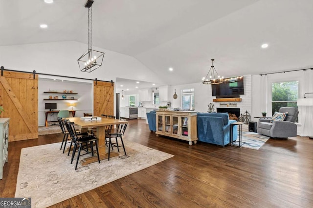 dining space with dark wood-style flooring, a barn door, a fireplace, a chandelier, and vaulted ceiling
