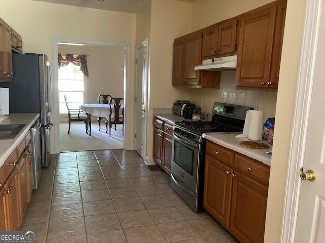 140 Cedar Creek Dr, Dublin, GA 31021 - kitchen with light tile patterned flooring, stainless steel gas stove, light countertops, brown cabinetry, and under cabinet range hood