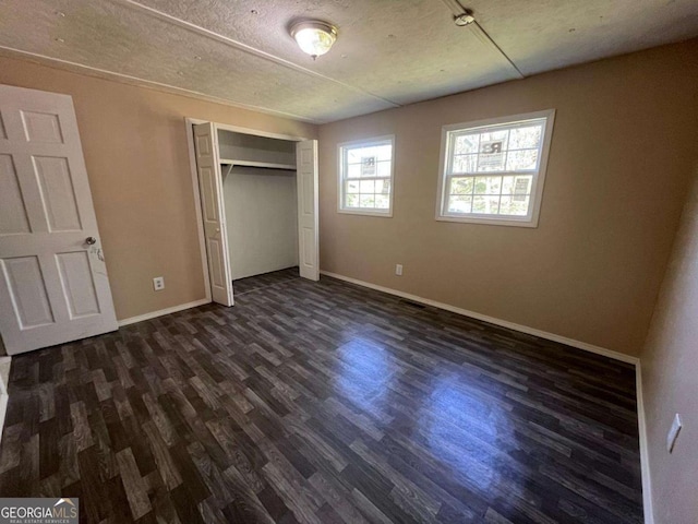 unfurnished bedroom featuring dark wood-type flooring, baseboards, and a closet