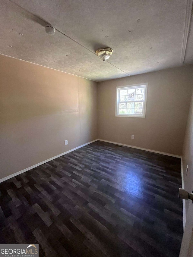 unfurnished room featuring dark wood-type flooring and baseboards