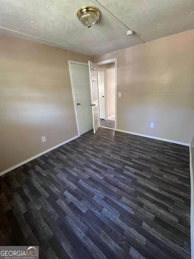 empty room featuring baseboards and dark wood finished floors