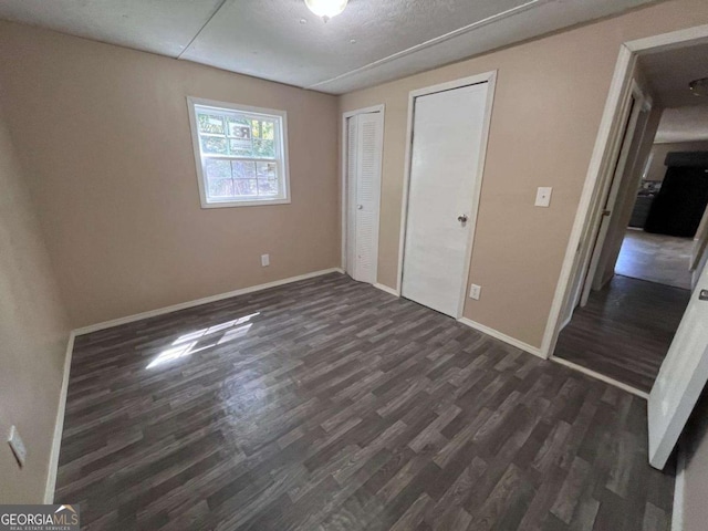 unfurnished bedroom featuring two closets, baseboards, and dark wood-type flooring