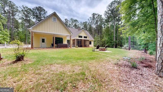back of house featuring a fire pit, a sunroom, board and batten siding, a lawn, and a hot tub