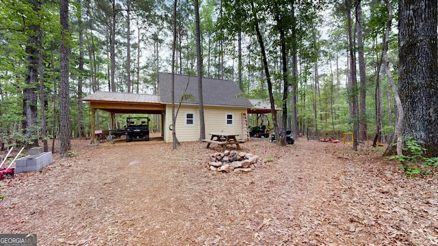 rear view of house featuring a shingled roof, dirt driveway, and a carport