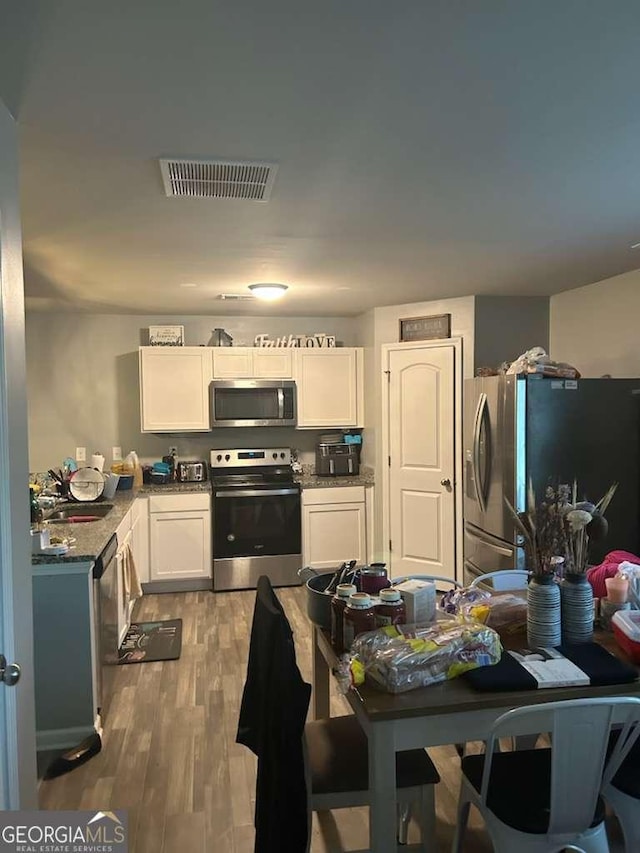 713 Dove Tree Ln, Social Circle, GA 30025 - kitchen featuring stainless steel appliances, light wood finished floors, white cabinetry, and visible vents