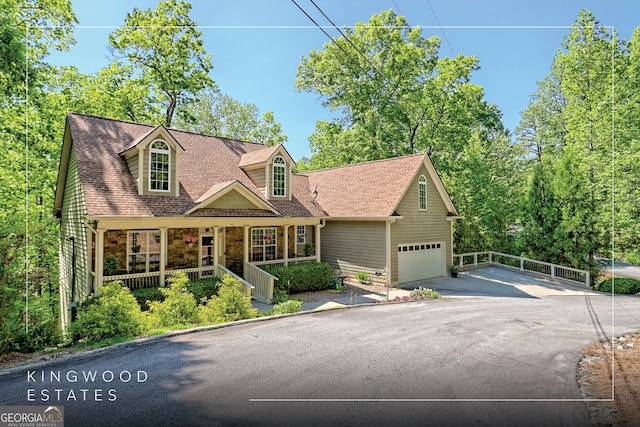 new england style home with covered porch, driveway, a garage, fence, and a shingled roof