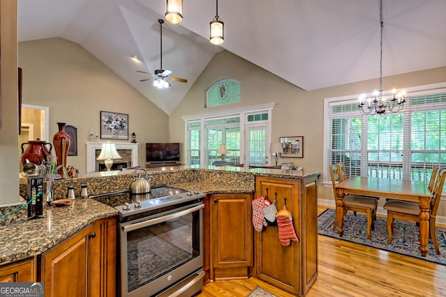kitchen with stainless steel range with electric stovetop, dark stone countertops, brown cabinets, light wood-style flooring, and ceiling fan with notable chandelier