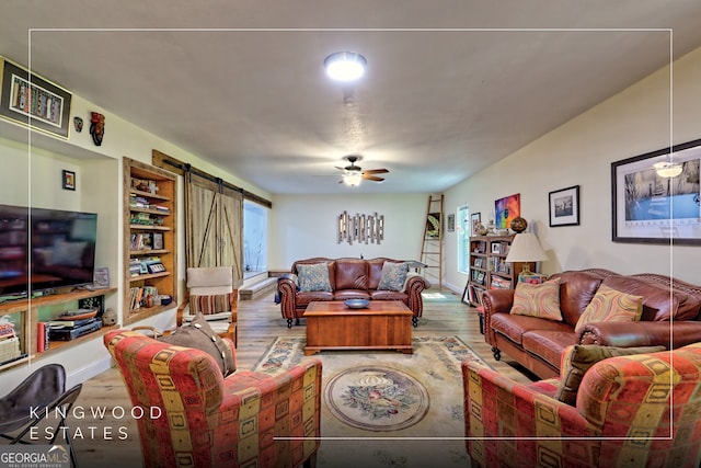 living area with a barn door, built in features, ceiling fan, and wood finished floors