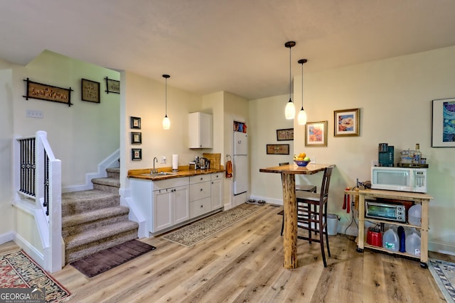 kitchen with pendant lighting, white appliances, light wood-style floors, white cabinets, and a sink