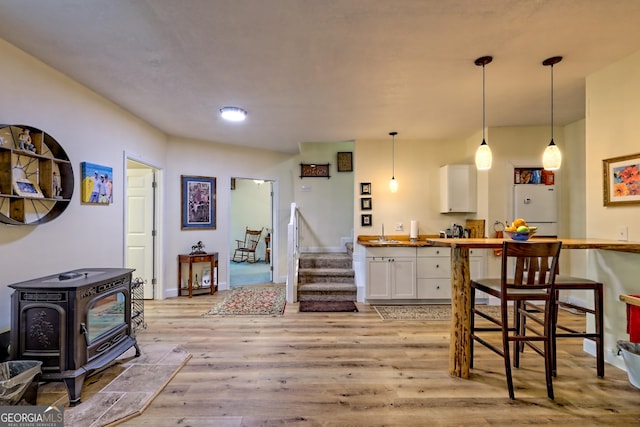 kitchen featuring a wood stove, light wood-style floors, freestanding refrigerator, white cabinetry, and decorative light fixtures