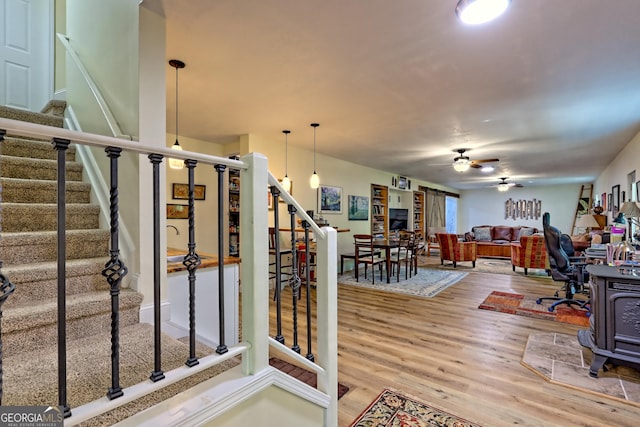 interior space with ceiling fan, a wood stove, stairs, and wood finished floors