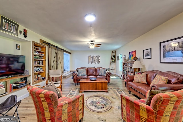 living room featuring a barn door, built in shelves, a ceiling fan, and wood finished floors
