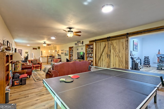 playroom with ceiling fan, a barn door, and light wood finished floors