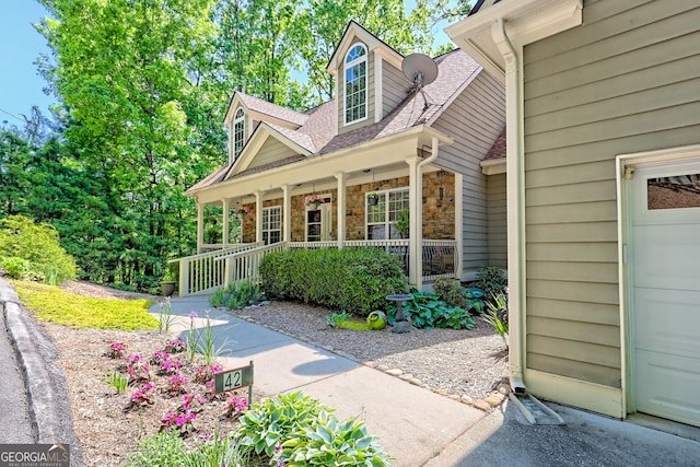doorway to property featuring a porch, a shingled roof, a garage, and stone siding