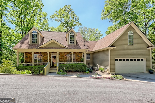 cape cod-style house featuring roof with shingles, stone siding, a garage, concrete driveway, and covered porch