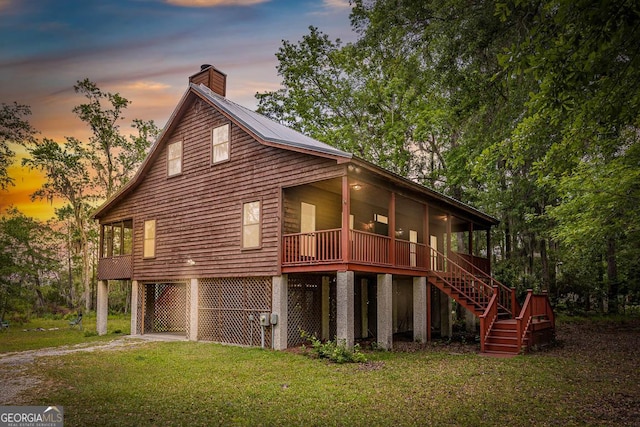 back of property at dusk with a porch, driveway, a chimney, a lawn, and stairway