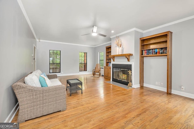 living room with light wood-style floors, a fireplace with flush hearth, ceiling fan, and ornamental molding