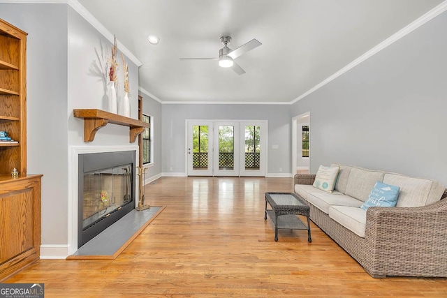living area with a ceiling fan, crown molding, baseboards, light wood finished floors, and a glass covered fireplace