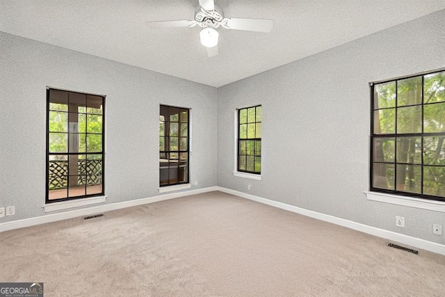 carpeted empty room featuring a healthy amount of sunlight, baseboards, and visible vents