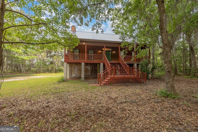 rear view of house with covered porch, a chimney, metal roof, a lawn, and stairway