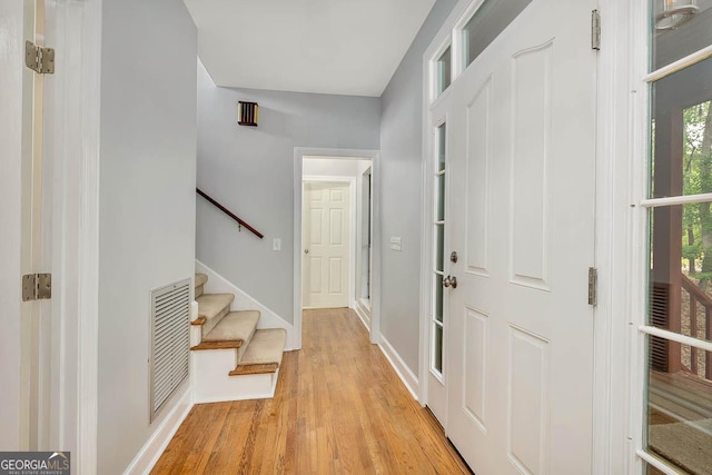 foyer entrance featuring baseboards, light wood finished floors, stairs, and visible vents