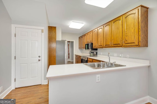 kitchen featuring a peninsula, light countertops, a sink, light wood finished floors, and stainless steel appliances
