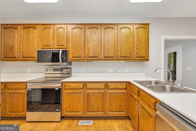 kitchen with visible vents, brown cabinets, a sink, stainless steel appliances, and light wood-style flooring