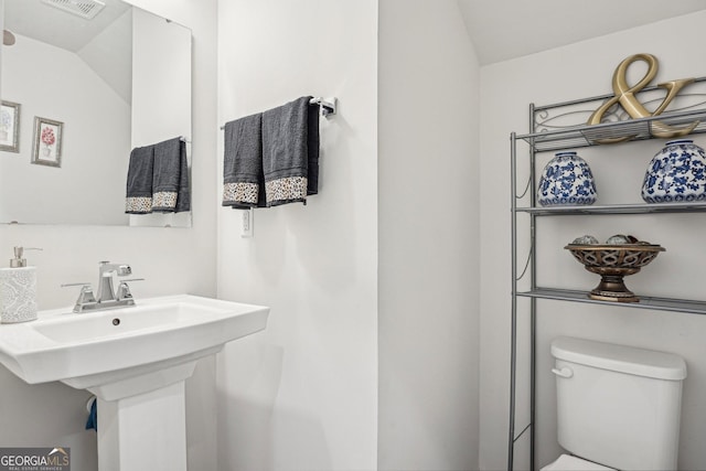 half bathroom with lofted ceiling, toilet, and a sink
