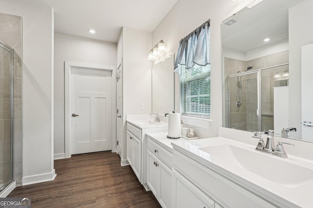 bathroom with a stall shower, wood finished floors, two vanities, and recessed lighting