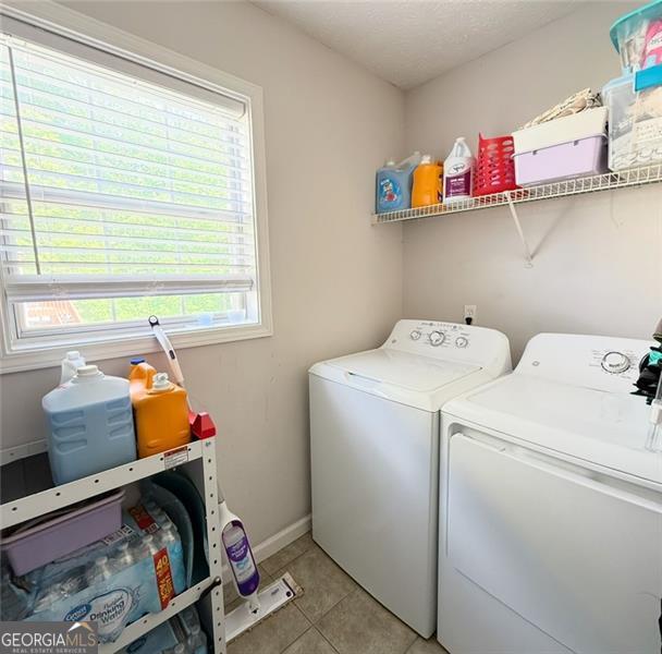 laundry area featuring laundry area, washer and clothes dryer, baseboards, and light tile patterned flooring