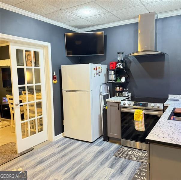 kitchen with gray cabinets, light wood-type flooring, stainless steel range with electric cooktop, freestanding refrigerator, and wall chimney exhaust hood