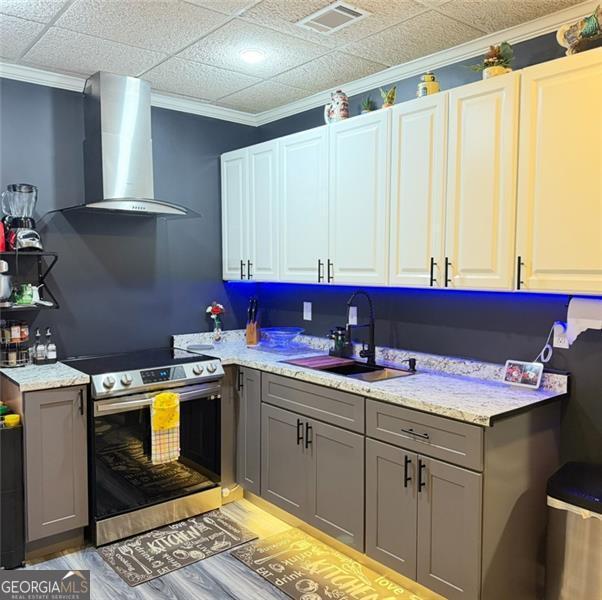 kitchen with gray cabinetry, wall chimney range hood, stainless steel electric range, and a sink