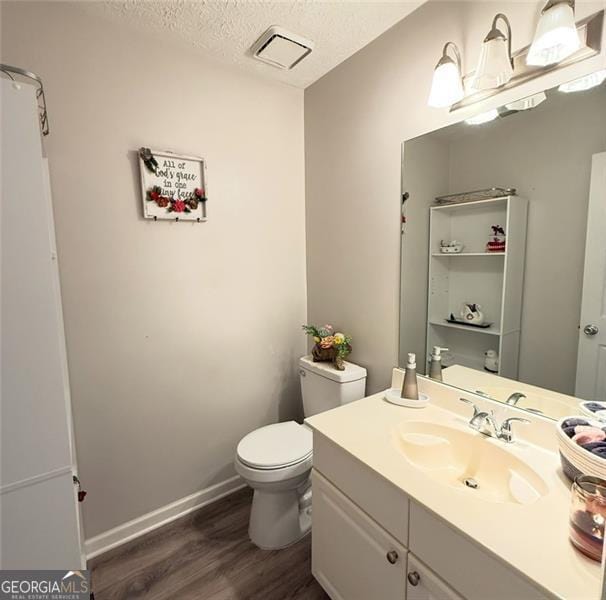 bathroom with vanity, toilet, a textured ceiling, wood finished floors, and visible vents