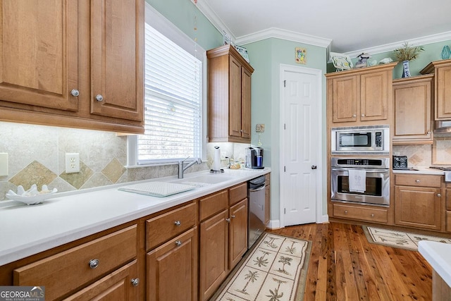 kitchen featuring crown molding, appliances with stainless steel finishes, wood finished floors, and light countertops