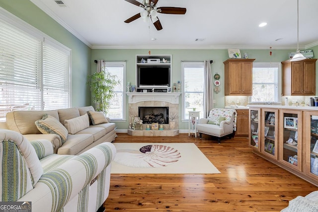 living room featuring ceiling fan, wood finished floors, a fireplace with raised hearth, ornamental molding, and recessed lighting