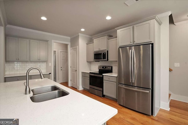 kitchen with stainless steel appliances, gray cabinets, ornamental molding, and a sink