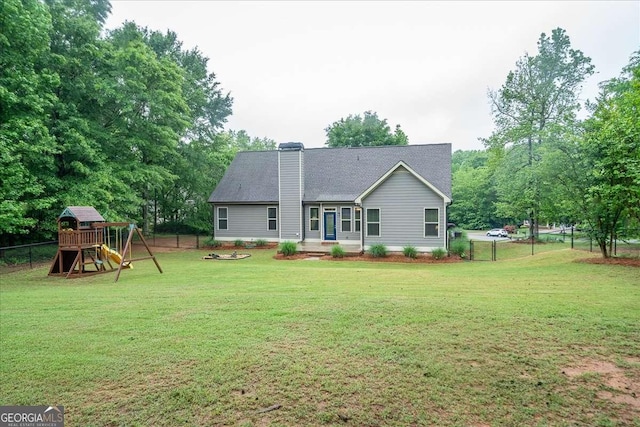 rear view of house featuring a playground, fence, a chimney, and a yard
