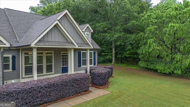 view of side of property with board and batten siding, roof with shingles, and a yard